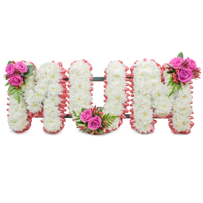 A poignant, bespoke floral display that spells the word MUM in large, connected capital letters, set against a pristine white background to emphasise its form and detail. Each of the three letters is lovingly formed from dense clusters of immaculate white chrysanthemums; the small, layered blooms are arranged so closely they produce a seamless, softly textured surface that appears almost luminous in gentle light. The outer contours of every letter are edged with a ruffled light-pink ribbon or fabric trim, which imparts a subtle rosy halo and a sense of tender care. Between the letters a dark green support frame is faintly visible, providing structural integrity for this upright memorial piece. To punctuate the whiteness, three neat arrangements of vibrant fuchsia-pink roses are integrated into the design - on the upper left of the first M, within the U's lower curve, and on the upper right of the second M - each accompanied by glossy fern-like greenery and clusters of small red-orange hypericum berries that lend texture and a soft, fruity counterpoint. The composition balances purity and warmth: chrysanthemums suggest solemn remembrance, while the pink roses and ribbon convey affection and gratitude. In the soft studio light used to photograph the piece, textures read clearly and the scent of roses would be quietly present. A local florist might recommend this style for services at nearby chapels or crematoria serving Canonbury, New River, or Islington, where families seek a dignified, personal tribute to a much-loved mother.