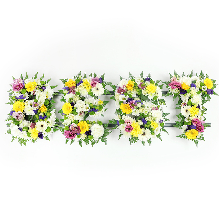 Bold yet tender, this floral composition spells BEST in four carefully shaped letters, photographed head-on on a luminous white background so every petal and leaf registers clearly. Each letter is composed of tightly clustered blooms - plush white chrysanthemum-style flowers form a soft, luminous foundation while bright yellow roses and gerbera bring a cheerful, sunlit tone. Interspersed are delicate mauve-to-purple lisianthus or small chrysanthemums, and lively magenta spray roses or petite carnations that add dainty highlights. Generous sprays of deep green fern fringe the perimeter of each letter, their feathered silhouette creating a natural border that contrasts with the vivid blossoms. Where the arrangement is most densely packed the floral surface reads seamless; in places such as the lower bar of the E and along the T you can glimpse the dark green or subtle metal framework holding the letters together, evidence of both floral artistry and engineering. The even, bright lighting renders colour and texture with clarity - velvety petals, crisp foliage, and the slight sheen of freshly cut stems all visible. The aroma is gentle: a faint mix of rose sweetness, green fern, and the clean, slightly spicy note of chrysanthemum. Crafted in the spirit of remembrance, this piece suits funerals, memorial services, or a personal tribute to someone recalled as the best. As Canonbury's local florists, Canonbury Flowers arranges and delivers these letter tributes around Canonbury Square, Essex Road, and into the wider Islington community with attentive care.