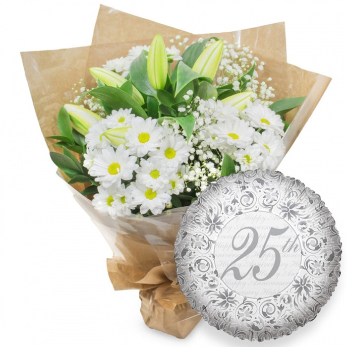 A carefully composed anniversary gift set is pictured against a pristine white background, highlighting every detail of the flowers and balloon with clarity and calm. On the left, a lush bouquet brings together white chrysanthemums, white lilies, and baby's breath in a timeless combination often chosen for 25th wedding anniversaries around Canonbury's elegant terraces. The chrysanthemums have neat, daisy-like faces with bright yellow centers that create a cheerful, hopeful mood, as if each bloom were a small burst of sunlight. Rising in and out of this cushion of daisies are elongated white lily buds, their pale petals still mostly closed, with just the suggestion of green at the tips and along the edges, capturing a moment of quiet anticipation before full bloom. Fine, cloud-like sprigs of gypsophila drift through the bouquet, softening lines and adding a romantic, whisper-light texture. Deep green leaves nestle behind and between the flowers, providing structure and a rich backdrop that emphasises the purity of the white petals. The stems are wrapped in a clear layer of cellophane, then swaddled in natural brown kraft paper whose slightly crumpled surface adds a warm, artisanal feel, similar to arrangements you might collect from a local Canonbury florist after a walk through nearby Highbury Fields. The base is securely tied, making the bouquet easy to carry to a celebratory dinner or intimate gathering. To the lower right, slightly overlapping the flowers, floats a round, metallic silver foil balloon. Its surface is adorned with ornate scrolls and floral motifs in a darker shade of silver, framing the central inscription 25th written in a graceful, semi-cursive script. Behind this, the words Happy Anniversary appear in softer grey, repeating like a gentle echo. The balloon's subtle crinkles catch the light, giving off small flashes that echo the understated glamour of a true silver anniversary celebration.