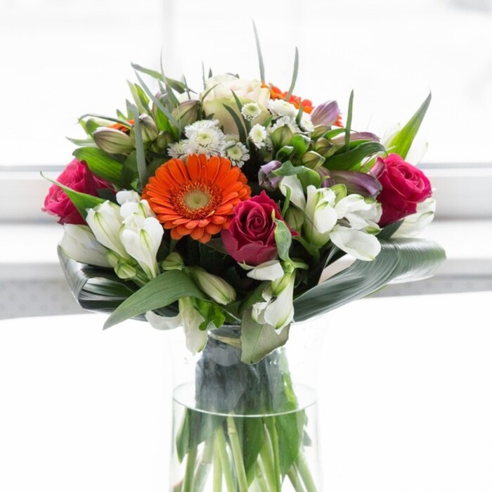 Grace and vibrancy intertwine in this expertly crafted bouquet, a testament to floral artistry found in the heart of Canonbury. Gentle peach gerberas encircle the arrangement, their dreamy petals softening the vivid energy of their orange counterparts. Deep fuchsia roses create pockets of aromatic luxury amidst a tapestry of cream-hued alstroemeria and dainty white buds, evoking an endless English summer. Lush, broad leaves wrap protectively around the stems, forming a natural collar reminiscent of the tranquil greenery in Canonbury's quiet crescents and gardens. Light washes over the arrangement, enhancing every nuance-from the velvet embrace of a rose to the subtle glint of dew on an aspidistra leaf. An almost rejuvenating freshness lingers in the air, prompting thoughts of early market mornings on Essex Road or leisurely lunches near the Regent's Canal. Whether gracing a celebratory table, decorating a friend's new home in N1, or extending wishes of happiness and hope, this bouquet's thoughtful composition assures each petal and stem tells a unique story-the story of care, optimism, and the vibrant community spirit that defines Canonbury.