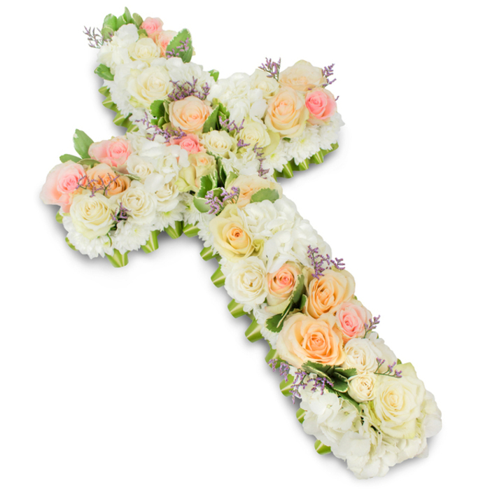 A beautifully composed Christian cross made entirely of flowers is displayed flat against a crisp white background, capturing the calm dignity of a traditional funeral tribute. The cross is lush and substantial, its arms thickly covered with layers of fresh blooms in a tranquil palette of white, ivory, soft peach, and gentle pink. Large, premium roses in creamy white and ivory form much of the underlying structure, their petals unfurling in graceful spirals. Interspersed among them are clusters of soft peach and blush-toned roses, some fully open and others still in bud, adding warmth and a sense of unfolding life along the central line of the cross. Fluffy white hydrangea clusters, or closely packed similar blooms, fill the spaces in between, creating a plush, cushion-like texture that feels both comforting and abundant. Here and there, tiny sprigs of lavender or pale purple filler flowers emerge, sprinkled sparingly like quiet notes of colour that enrich rather than overpower the design. Fine touches of fresh green foliage peek from beneath the blossoms, particularly along the edges, giving the cross a gently defined outline and subtle depth, reminiscent of the greenery around Canonbury's squares and gardens. The lighting is bright and even, casting only the softest shadow beneath the arrangement to emphasize its three-dimensional form. Crafted with the care of a skilled local florist, this floral cross would be a fitting centrepiece at a Canonbury funeral, memorial, or church service, conveying faith, remembrance, and a heartfelt farewell to a loved one.