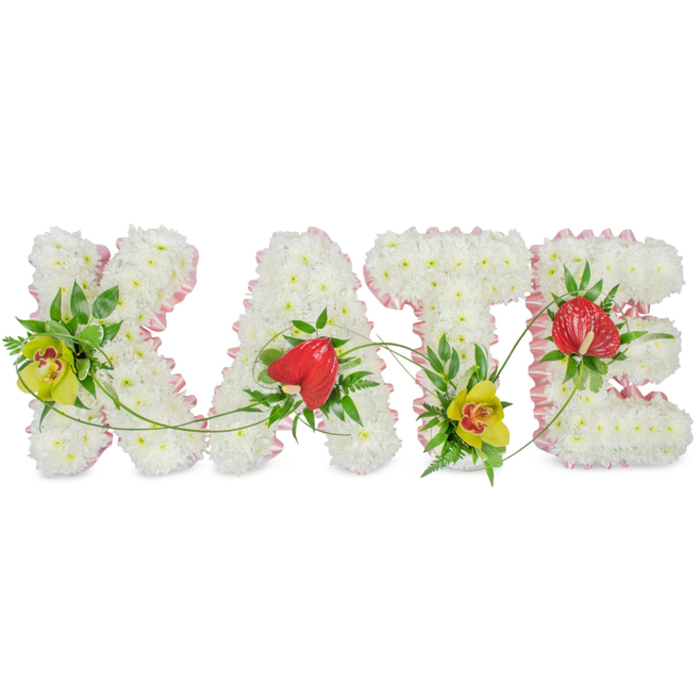 This photograph captures a dignified floral name tribute spelling KATE, designed as four individual capital letters, each one dense with snowy white chrysanthemums that form a soft, cushion-like surface. The flowers are tightly packed so that no gaps show, giving every letter a solid, reassuring presence, as though each petal contributes to a single, united expression of love and remembrance. Around the outer outline of the K, A, T, and E runs a light pink satin ribbon, gently pleated and pinned to follow the curves and angles, providing a delicate pastel frame that softens the otherwise crisp white forms. Resting on a bright, uncluttered white background, the arrangement appears calm and composed, much like a peaceful corner of Canonbury's quiet residential streets. Within the letters, rich green foliage has been artfully tucked in, providing depth and contrast. On the left stroke of the K and near the foot of the T, striking lime-green cymbidium orchids with warm reddish-brown centres emerge, their broad petals and exotic markings adding both elegance and a contemporary note. On the crossbar of the A and along the top of the E, glossy red anthuriums with their distinctive heart-shaped, waxy bracts lend a bold symbol of affection and devotion, echoed by surrounding leaves and slender fern fronds. Fine green tendrils arc and curl between the letters, subtly tying them together. This custom floral tribute, suitable for funerals and celebrations of life in Canonbury and nearby Islington, reflects the skilled hands and sensitive design choices often sought when families commission personalised memorial flowers.