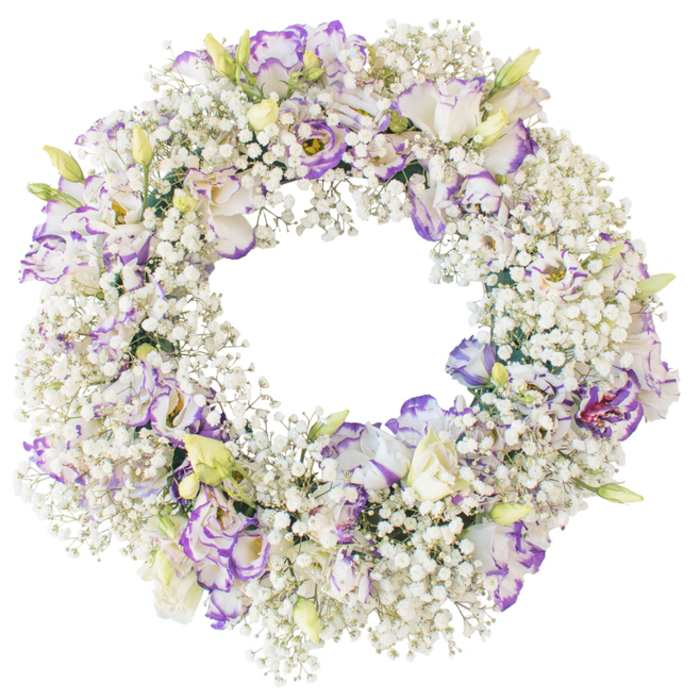 A meticulously crafted funeral wreath is photographed against a crisp white backdrop, its circular design evoking both softness and structure. The outer and inner edges are generously filled with white Baby's Breath, creating an almost feathery halo made up of innumerable tiny blossoms that collectively resemble a gentle, floral snowfall. These Gypsophila sprigs arch and interlace, giving the wreath a plush, cloud-like volume that is especially striking in the clean, even light. Nestled deep within this airy texture are clusters of Lisianthus blooms, placed with care so that each one has space to open and be admired. Their petals unfurl in layers, starting from a creamy white heart and gradually meeting fine tracings of lavender and rich purple along the margins, as if dipped in colour. Some flowers are in full, ruffled bloom, while others are captured at earlier stages-buds that are pale green at the base, with tips just beginning to show hints of the violets and whites within. The open centre of the wreath forms a calm, circular window, a visual reminder of continuity and eternal love, making the design especially suited to farewell services, memorials, or graveside vigils around Canonbury's tranquil residential streets. The colour harmony of cool white and soft purple conveys peace and heartfelt respect, without any bold or jarring tones. With no visible foliage beyond a few discreet green stems, the focus remains squarely on the flowers themselves. It feels like the sort of gentle, dignified tribute a local Canonbury family might choose when asking a trusted florist in the area to create something quietly beautiful in honour of a loved one.