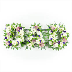A thoughtfully composed funeral flower tribute spells out DAD in three bold capital letters, arranged in a neat horizontal line against a clean white background, like a quiet pause in the midst of grief. Each letter is built on a generous base of white blooms: plump chrysanthemums, open-faced gerbera-style daisies, and small white spray roses cluster side by side, creating a plush, almost quilted texture that appears soft to the touch. Between the petals, you can almost imagine the faint, fresh scent of early morning flowers from a Canonbury garden after rain. The shapes of the letters are defined and softened by abundant greenery, primarily airy fern fronds and other lush foliage that weave around the contours, framing the white flowers in a fresh, lively green. Tucked within the white are restrained, meaningful touches of colour - deep purple blossoms that resemble violas or pansies, and clusters of violet and plum-toned chrysanthemums or carnations - bringing an air of quiet dignity. Here and there, rounded buds and open blooms of lavender and pale mauve roses add a gentle, nostalgic warmth, as though reflecting shared stories and memories. The lighting is bright but not stark, akin to natural daylight in a Canonbury studio, revealing all the fine details of each bloom while keeping the mood serene. This floral DAD tribute is designed for a funeral or memorial service, suitable to be delivered to local churches or chapels, and would sit gracefully beside family wreaths or sprays. It conveys respect, love, and a heartfelt final thank you to a much-loved father, created with the care and craftsmanship of an experienced local florist.