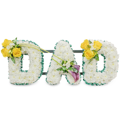 A carefully composed floral tribute that spells DAD in rounded, generous block letters, each formed from a dense carpet of pristine white chrysanthemums whose clustered florets create a soft, pillowy surface. The letters are subtly defined by a ruffled dark-green ribbon that traces the edges like a quiet frame, the contrast giving the arrangement a composed, dignified presence against a bright white backdrop. Scattered across the composition are clusters of sunlit yellow roses paired with creamy freesia sprays; their warm colours and gentle perfume evoke sunlit afternoons and the easy laughs of remembered days. At the heart of the A, a pair of stately calla lilies - one with a faint lilac wash - rise with sculptural grace, their trumpet forms lending an air of refined hope and solemn beauty. Two long, bare green stems sweep diagonally from the left cluster toward the centre, introducing a sense of motion and connection between letters. Slim dark-green metal supports peek from behind, giving the display necessary strength while keeping the focus on flowers and feeling. Presented as a memorial piece for a father or paternal figure, this arrangement balances purity and warmth: white for peace, yellow for fond remembrance, and purple for reverence. As a florist familiar with Canonbury and the streets around Essex Road and Upper Street, I picture this resting near a funeral chapel or simple family service, a handmade expression of respect that reads clearly from a distance yet invites close, comforting inspection.