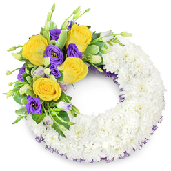 This circular funeral wreath is sculpted from hundreds of small, immaculate white spray chrysanthemums to form a continuous, serene ring photographed against a clean white ground. The tightly clustered blooms create a smooth, pillowy surface whose layered petals suggest softness and repose. On the upper left arc a considered cluster of colour emerges - bright yellow roses, their petals unfurled like small suns, paired with rich purple lisianthus whose satiny, ruffled cups provide a cool, dignified counterpoint. Unopened lisianthus buds in pale lavender and soft green introduce subtle depth, and an assortment of fresh greenery - glossy round leaves, narrow ferny fronds and a few variegated stems - frames the spray, giving it lift and organic flow. A thin, dark purple mesh ribbon is partially revealed beneath the white blooms, tracing the wreath's inner edge and linking visually to the purple flowers above. The lighting is gentle, revealing the chrysanthemums' texture and the roses' soft fragrance without dramatic shadows. As a composition intended for memorial use around Canonbury - perhaps at small services by New River Walk or for quiet tributes near Upper Street - it conveys calm dignity, purity and a warm note of remembrance. The craftsmanship reads as thoughtful and precise, designed to comfort and honour in equal measure.