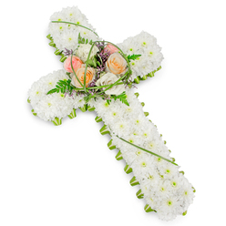 A traditional Christian cross made entirely of flowers is shown against a clean white backdrop, the design capturing the quiet, reflective spirit often felt along Canonbury's residential lanes. The body of the cross is densely packed with small white cushion chrysanthemums or similar blooms, placed so closely that they create a seamless, soft surface, like freshly fallen snow resting in stillness. Their bright whiteness conveys purity and peace, ideal for a farewell tribute. Around the outer edge, a narrow band of bright green foliage traces the full outline of the cross, from the top arm right down to the base. This precise green border gives clear definition to the shape, drawing the eye and framing the white petals with a natural, living contrast that feels reminiscent of the leafy verges of nearby New River Walk. At the centre where the cross's arms meet, a delicate focal spray of larger flowers rises gently from the surface. Several roses in harmonious, warm tones-soft peach, pale pink, and creamy white-are arranged to form a tender cluster, their open blooms suggesting compassion, comfort, and cherished memories. Around them, feathery fern leaves extend outward, and fine strands of bright green grass curl and loop, adding a sense of movement and grace. Small touches of purple filler flowers peek through the greenery, introducing a quiet accent hue that enriches the composition without overwhelming it. The lighting appears diffuse and calm, with the white background eliminating distractions and focusing all attention on the tribute itself. This floral cross arrangement, like those often prepared for local services by Canonbury Flowers, is suited to funerals or memorials, offering a soothing symbol of faith, remembrance, and the hope of peace.