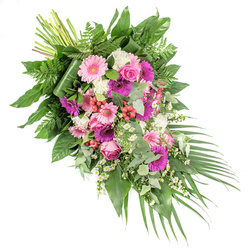 A refined sympathy spray stretches diagonally across a white backdrop, beginning with a tight cluster of stems at the upper left and flowing downwards into a soft cascade of colour and foliage at the lower right. The arrangement is rich yet gentle, woven from a palette of blush pink, fuchsia, mauve, deep purple, and bright white, all resting on a bed of layered greens. Large gerbera daisies in dusky pink and saturated magenta form the main focal points, their wide petals radiating around dark centres like soft, open faces. Between them, pink roses unfurl with poised grace, their spiralled hearts creating a sense of calm and continuity. Around these sit fluffy white blooms-carnations or mini chrysanthemums-offering a downy texture that lightens the overall look. Scattered throughout, clusters of tiny white daisy-like flowers lend a playful yet tender touch, reminiscent of wildflowers along the paths of New River Walk in Canonbury. Small sprays of red hypericum berries peep out between leaves, adding discrete flashes of warm colour and berry-like shine. The foliage framework includes broad, lacquered dark green leaves, light and feathery ferns, and soft, rounded eucalyptus in a silvery green that suggests a refreshing scent. Arching palm leaves taper the design at the lower right, reinforcing its sweeping, diagonal motion, well suited to lie on a casket or stand as a prominent tribute. The lighting is soft and even, bringing out subtle variations in tone and texture. Crafted with care by local Canonbury florists, this funeral spray is designed to convey compassion, peace, and heartfelt remembrance at services throughout the area.