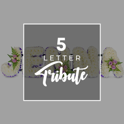 In this detailed image, a bespoke five-letter funeral flower tribute is displayed against a smooth, light grey surface, reminiscent of the quiet, understated interiors of Canonbury's small chapels and community spaces. Each individual letter is built on a sturdy frame and entirely covered with pristine white chrysanthemums, the blossoms packed so closely that they form a velvety, almost quilted surface. The edges of the letters are carefully finished with a deep purple satin ribbon, folded and pinned into place so that it creates a neat, continuous outline, adding both structure and a gentle sense of ceremony. Soft clusters of accent flowers are positioned thoughtfully along the letters: delicate pale pink and mauve spray roses peep out between the white blooms, interwoven with fresh green fern fronds and small leafy sprigs. These pastel touches bring a hint of colour and softness, suggesting memories that are tender rather than heavy. The arrangement itself spells out a name, with the letters "J," "O," "H," and "N" visible, followed by an "A" at the far right, although a central square overlay partially obscures them. This overlay, in a slightly darker shade of grey, is framed by a slim white border and carries the words "5 LETTER" in crisp white capitals, above the word "Tribute" in an elegant script. The lighting is even and gentle, with no harsh shadows, allowing every petal and ribbon fold to be seen clearly, as if a Canonbury florist were quietly showing a family the kind of personalised letter tributes that can be created for a memorial service or crematorium farewell.