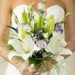 Imagine a Canonbury morning: soft light filtering into an elegant Islington flat, a bride poised in anticipation, holding a bouquet that seems to float with emotion. Broad, creamy white lily blooms open generously, surrounded by unopened buds whispering of moments yet to bloom. Feather-light wisps of baby's breath and airy green fern add a dreamlike, ethereal touch, conjuring the atmosphere of nearby New River Walk on a misty spring day. Surprising pops of lavender-edged lisianthus swirl among the lilies, edges ruffled with a playful elegance as if touched by watercolour-hints of purple reminiscent of wisteria climbing Canonbury villas. The entire bouquet is expertly gathered, designed for movement and harmony, its stems wrapped and held by hands with delicate, light-hued polish. Fragrance drifts in gentle waves: lacy lilies mingling with clean, dewy foliage, stirring feelings of purity, renewal, and the radiant joy of a wedding day. Assembled with heart by Canonbury's local florists, this arrangement is more than flowers-it's a poetic expression of hope, artistry, and joyous anticipation, perfectly suited for North London's most memorable celebrations.