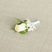 At the centre of this boutonniere rests a pristine ivory rosebud, its petals layered with a velvet softness that invites a closer look. Small clusters of cloud-like baby's breath cradle the bloom, their tiny white stars softening the composition, while slender, feathery sprigs of dark green foliage-reminiscent of cedar-reach outward, providing a graceful, textured silhouette against broader, deep-green leaves that offer a steady, structural backdrop. The stems are wrapped in a satin-white ribbon, its sheen discreet and refined, tied into a tidy bow that anchors the arrangement and speaks to meticulous hand-tying techniques. Placed on a subtle light-beige woven fabric, the boutonniere's tones are amplified: the creamy petals, bright white gypsophila, and varying greens read with clarity and calm under soft, diffused light.

As a florist who daily walks Canonbury's streets and sources seasonal stems from nearby markets, I find this small piece particularly suited to intimate ceremonies around Essex Road and the Angel. It carries a delicate fragrance-fresh, faintly floral-evoking the early hours before a celebration. Practical yet poetic, the boutonniere is cut and prepared to last through vows and photographs, intended to be worn close to the heart. Available through Canonbury Flowers for local occasions, it's a traditional, timeless choice that balances purity and craftsmanship, perfect for grooms, ushers, or anyone who prefers quiet sophistication over flourish.