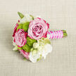 A small, exquisitely composed bouquet lies gently on a textured, light beige fabric that resembles natural linen or burlap, the neutral surface providing a calm, earthy backdrop like the pale interiors of a Canonbury mews home. At the centre of the design are two large, perfectly formed roses, their petals arranged in tight, layered spirals. The colour moves from a soft, blush-pink at the core to a richer fuchsia and magenta along the outer edges, creating a luminous gradient that suggests both tenderness and drama. Nestled around these roses are lime-green button chrysanthemums, their rounded, compact heads made up of countless minuscule petals that offer a lively, almost playful contrast to the smooth rose petals. Delicate white flowers are woven through the composition, some fully opened with slender petals surrounding subtle yellow-green centres, others closed into creamy buds that add poise and softness. Fine green stems and leaves peep through here and there, lending a sense of natural movement while keeping the overall shape tight and intentional. The stems are trimmed short and bound into a neat handle, which is beautifully wrapped in a satin-finished fuchsia ribbon that looks cool and silky to the touch. Winding elegantly over this ribbon is a fine strand of pearl-like beads, each one catching the light like tiny droplets, giving the bouquet a sense of celebration fit for a registry office ceremony off Upper Street or an intimate garden wedding near Canonbury Square. The arrangement feels fresh, modern, and romantic, ideal as a boutonniere, wrist corsage, or petite bridesmaid posy for special moments shared in North London.