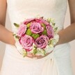 In the soft dawn light filtering over Canonbury's leafy streets, a bride gently cradles a round, luminous bouquet, its hues and textures capturing the poetic promise of a wedding morning. Velvety roses, blooming at the bouquet's center, melt from pale mauve to a dusky fuchsia at their petal tips-each flower an echo of the serenity found in local gardens just after rain. Lime-green button chrysanthemums nestle among the roses, their vibrant freshness a joyful surprise and a nod to the lively community parks nearby. This heart of lush colour is circled by a dreamy halo of delicate white-perhaps sweetly scented freesia or petite spray roses-giving the bouquet softness and a whisper of classic bridal tradition. Tender green shoots and buds thread through the composition, adding quiet organic detail. The bride's hands, nails glossed a gentle blush and a dusting of shimmer, hold the bouquet with reverence, while the intricate lace of her dress weaves subtle patterns of light around her. Each element-petal, stem, lace-melds into a vision of calm beauty, as if time has paused at the threshold of her new life. The scene feels deeply rooted in Canonbury's romantic charm, a testament to the thought and care local florists bring to each bridal design, ideal for couples seeking an elegant floral statement woven with the spirit of their neighbourhood.