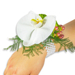 A delicate wrist corsage rests gently on a fair-skinned wrist against a pristine white background, every element arranged to read clearly in soft daylight. The focal bloom is a single, large white Phalaenopsis orchid with broad, satiny petals that unfold like a small, quiet fan; its lip shows a concentrated splash of warm yellow edged with deeper orange, drawing the eye to the flower's sculpted centre. Beneath and around the orchid, airy sprigs of asparagus-type fern form a feathery green cushion, their fine texture contrasting with the orchid's smooth surface and lending a soft, natural silhouette. To the upper right, a compact cluster of Hypericum berries introduces a seasonal shift in colour: pale green at the base graduating through rose to a cranberry red, the glossy rounds catching light like tiny, ripe jewels. A touch of lime-green ruffled foliage near the berries adds a crisp accent and another layer of texture. The whole composition is secured on the wrist by a classic multi-strand bracelet of small white pearls, their cool lustre nestling against skin and echoing the orchid's purity. The arrangement reads as timeless and romantic, suited to weddings, proms, or quiet celebrations, and the clean white backdrop ensures every nuance of colour and craft is visible. As a local florist might note while delivering to Canonbury Square or along New River Walk, the corsage combines fresh floral perfume, gentle tactile contrasts, and careful wiring so it feels as comfortable as it is elegant, a small but memorable piece of floral jewellery for a special day.