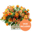 A richly layered bouquet in warm orange, golden yellow, and soft peach tones is photographed against a crisp white background, evoking the cosy glow of an autumn afternoon in Canonbury. The eye is first drawn to the cluster of large orange roses, some with petals that shift gently to yellow near the center, their open, velvety blooms giving a sense of generosity and welcome. Alongside them sit bright yellow garden-style roses, tighter in form and intricately ruffled, adding structure and a classic charm. Threaded between these focal flowers are numerous stems of peach and light orange alstroemeria, their slim petals delicately streaked and speckled, bringing a graceful, airy rhythm to the arrangement. Dotted throughout are small, vividly coloured spherical orange flowers, spiky and thistle-like in texture, which introduce an element of playful contrast against the softness of the roses and lilies. A lush frame of greenery encircles the blooms, including broad, silvery eucalyptus leaves and deeper green foliage, creating a cool, fresh backdrop that makes each warm petal stand out more vividly. The bouquet is carefully composed in a clear square glass vase, allowing the lines of the stems and the water level to be easily seen, giving a reassuring impression of freshness and expert care. Around the middle of the vase, a strip of natural beige burlap or jute is wrapped snugly, adding rustic charm that would feel perfectly at home on a kitchen table off St Paul's Road or a living room shelf near Canonbury Overground. In the bottom right corner of the image, a circular orange badge with bold white capital letters reads VASE INCLUDED, indicating that the arrangement arrives exactly as shown, a ready-made gift ideal for birthdays, thank you gestures, or brightening a home with same-day local flower delivery in N1.