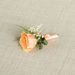 Delicately styled and photographed from above, this buttonhole features a single apricot-peach rose whose petals unfurl in tight, velvety spirals; the colour subtly shifts from deeper orange at the heart to softer, cream-tinged edges, evoking the last glow of a summer sunset. Nestled close to the rose, clusters of pure white baby's breath (Gypsophila) lend a light, almost cloud-like counterpoint, their tiny blossoms catching light and casting gentle, lace-like shadows on the textured background. Two rolled, darker green leaves tuck in behind the bloom with a tailored, almost folded appearance, while fine, bright green grass blades add vertical movement and fresh contrast. The stems are expertly bound in a coordinating peach satin ribbon tied into a neat, understated bow and finished with a small metallic pin-practical for attaching to a groom's lapel or a prom jacket. The arrangement sits on a neutral, woven taupe-ecru fabric that reads like natural linen, its soft cross-hatch texture providing a quiet backdrop that elevates the boutonniere's tones and craftsmanship. There's a gentle sense of occasion here-this is a piece designed for vows exchanged under soft daylight or for photographs taken along Canonbury's tree-lined streets. As someone who arranges flowers for local couples and families, I picture this boutonniere pinned on the lapel while guests stroll from Newington Green to Upper Street, carrying the intimate scent of rose and summer air.