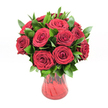 A lush, romantic bouquet of twelve to fifteen deep red roses is gathered in a translucent ruby glass vase, photographed cleanly against a pure white background so every detail stands out. Each rose is fully open, the velvety petals curling into perfect spirals that layer upon one another, creating a sense of depth and richness you can almost feel with your fingertips. The blooms are a saturated crimson, the sort of intense red that instantly suggests passion, devotion, and timeless romance, like a quiet evening stroll through Canonbury's leafy streets on Valentine's night. Between the roses, generous stems of dark, glossy green foliage, likely ruscus, weave in and out, their pointed leaves providing a fresh, verdant frame that makes the red appear even more vivid. The foliage adds body and structure, giving the bouquet a full, rounded silhouette that feels both luxurious and natural. The vase itself is a striking feature: a red glass vessel with gently curving sides that narrow towards the base, then flare softly at the top. Its subtly ribbed or undulating texture catches the light, causing streaks and highlights to ripple through the glass and echo the swirling form of the rose petals. Because the glass is translucent, hints of darker and lighter red appear where the stems meet the water, tying the arrangement together in one harmonious palette. Bathed in even, studio-style lighting, every petal edge and leaf vein is crisply defined, making this bouquet ideal for evoking love, anniversaries, or heartfelt celebrations in Canonbury homes, from elegant terraces near New River Walk to cosy flats tucked just off Essex Road.