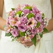 The bouquet, held lightly by a bride in a soft white gown, feels like a fresh promise-a blend of tender lilac and blush roses, lively green button mums, and delicate pink alstroemeria reflecting the carefree elegance Canonbury is known for. The roses open with a gentle fragrance, their petals luminous, while lime green chrysanthemums punctuate the bouquet with playful, spherical accents, lending modern brightness to the design. Pink alstroemeria lilies, graced with subtle maroon and yellow striations, whisper of distant gardens and joyous memories. Sprays of white baby's breath float like early morning mist, infusing the ensemble with lightness and quiet joy. Deep green leaves arc around the blooms, creating a natural, inviting frame. This nuanced arrangement, perfect for an Islington wedding or celebration by Newington Green, radiates hope and artistry in every detail-an authentic Canonbury design embodying both the grace of tradition and the vibrancy of new beginnings.