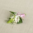 A delicately handcrafted boutonniere rests on a softly textured, light beige fabric that looks a little like natural linen laid out on a Canonbury dressing table. At the heart of the design sits a single, open white alstroemeria bloom, its broad petals slightly ruffled at the edges and finely brushed with reddish-brown speckles near the throat, creating a gentle focus for the eye. Tucked just to the side is a striking lime-green conical spike of tightly packed buds, their scale-like texture adding sculptural interest and a sense of budding life, as if caught a day before they fully open. Around these focal elements, tiny clouds of white baby's breath drift through the composition, their minute blossoms giving a feather-light, almost misty softness that bridges flower and foliage. The greenery beneath is carefully layered: broad, dark, spear-shaped leaves provide a sturdy base, while slimmer grass-like blades arc and weave, introducing a feeling of movement and airy texture. A narrow satin ribbon in a clear, cheerful pink is tied into a neat, compact bow at one end, its glossy loops catching the even, natural light and adding a playful hint of colour against the calm whites and greens. The lighting is soft and balanced, with no harsh shadows, highlighting the freshness of every petal and leaf. The overall impression is of a quietly elegant buttonhole or small corsage, perfect for a Canonbury wedding ceremony near Highbury Fields or a formal celebration along Newington Green, ready to be pinned to a lapel or fastened to a wrist as a subtle, refined accent.
