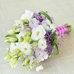 Intricately hand-tied on a soft, neutral linen backdrop, this Canonbury-inspired bridal bouquet radiates refined elegance and contemporary charm. The main attraction is the array of creamy white Lisianthus blooms, their delicate ruffles blooming alongside buds of fresh pale green, each petal whispering of spring's arrival in the leafy streets around Canonbury Square. Deep purple, star-shaped allium florets inject vibrant energy and modern texture, while pastel lavender and pink accents from companion stock flowers enhance the feeling of soft romance and tranquil joy. Interwoven among the arrangement, slender blades of green and varied buds create an impression of organic movement-mirroring the gentle sway of local tree canopies and the energy of community gardens. The bouquet is expertly gathered and finished with a bright fuchsia ribbon, tightly securing the fresh stems and accented by a lustrous pearl strand for a sophisticated, celebratory finish. Echoing themes of new beginnings, artistry, and devotion, this bouquet brings a taste of Canonbury's serene beauty and expert floristry to any wedding or special occasion, perfect for anyone drawn to the area's blend of history, greenery, and understated luxury.