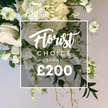 A lush, white-and-cream floral spray rests against a soft ivory backdrop, as if staged for a quiet corner of Canonbury. The arrangement gathers a rich chorus of blooms: creamy white roses in both velvet, almost unfurled blooms and tight buds; voluminous clusters of hydrangeas that feel like cloud-soft mounds; and slender white sweet peas gracefully trailing downward, their stems adding a slow, downward sweep. Interwoven are Nigella flowers, Love-in-a-Mist, with delicate, spiky green centers and feathery foliage that give a touch of whimsy. The greens vary from broad, deep-toned leaves to lighter variegated ones and wispy tendrils that soften the silhouette. A few rustic, thin woody stems emerge from the base, lending a natural cascade to the arrangement. In the center, a crisp white rectangular frame overlays the bouquet. Within it, the script proclaims Florist Choice, while beneath in uppercase sans-serif the word SPRAY announces the product type. At the bottom, bold numbers read ?200, as if captured from a storefront display. The overall presentation radiates premium craftsmanship, a versatile white spray suited for remembrance, celebration, or elegant decor. The soft, light beige backdrop enhances the purity of the whites and greens, and the composition exudes calm, restraint, and refined luxury. This image would sit well on Canonbury's shop pages, signaling to locals across Upper Street, Newington Green, and Essex Road that the same-day delivery from Canonbury Flowers can bring this classic spray to doors nearby.